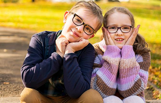 Two children sit outside, leaning toward each other playfully 