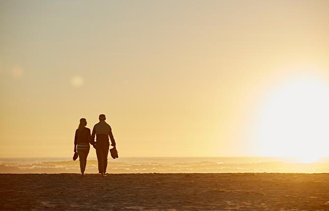 Two people walk hand in hand on the beach at sunset. 