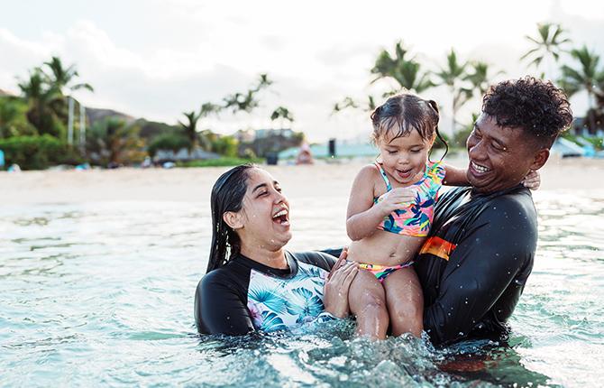 A woman and man hold a young child, swimming and laughing. 