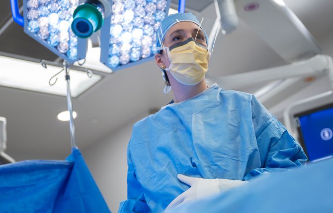 A cancer doctor in surgical scrubs and a face mask stands in an operating room at MSK. 