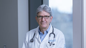 A doctor with gray hair and glasses, wearing a white coat and stethoscope.