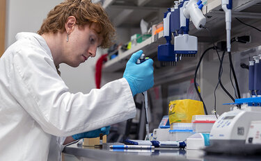 An MSK scientist in a lab holding a pipette over at test tube. 