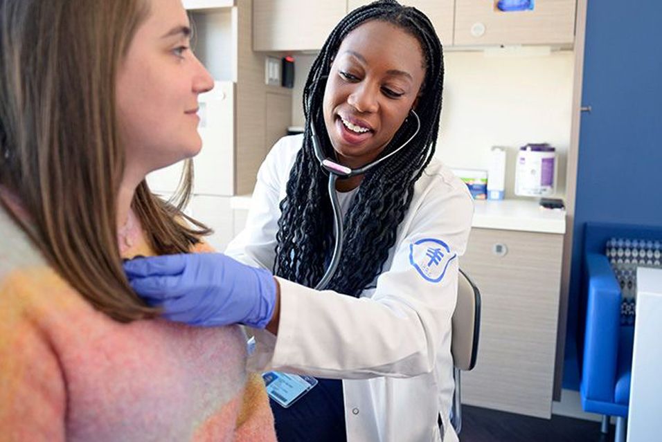Doctor using a stethoscope on a patient, smiling warmly in a medical office.