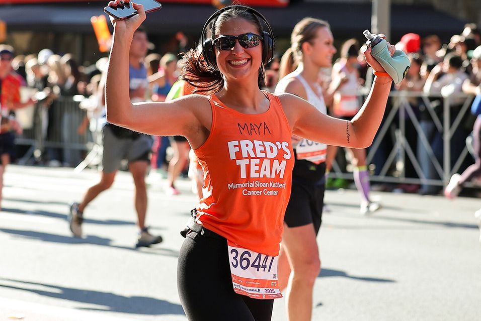 Runner in orange top and sunglasses smiling, during a race.