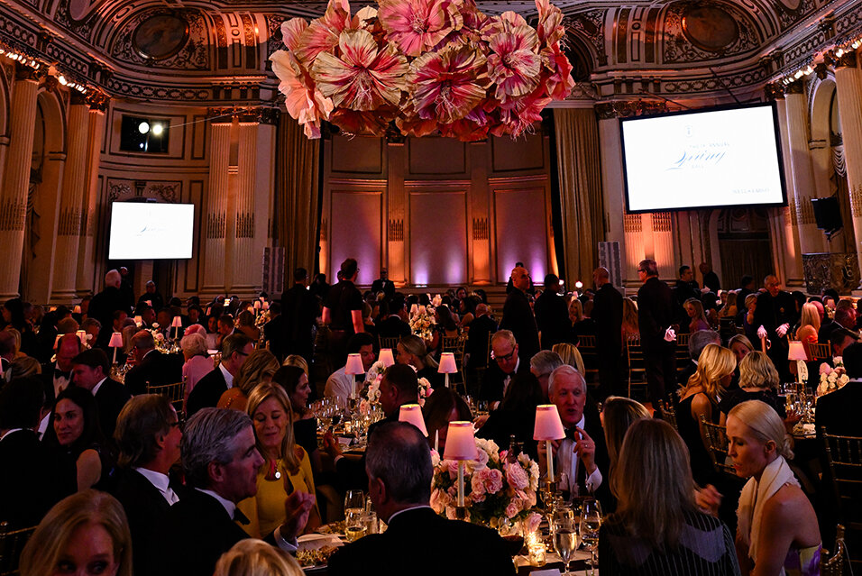 Society Members and guests seated at tables and enjoying dinner at the Spring Ball. A large, pink floral installation hangs from the ceiling in the center of the ballroom.