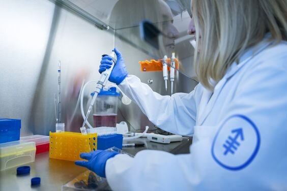 Scientist in lab coat uses pipette in laboratory setting.