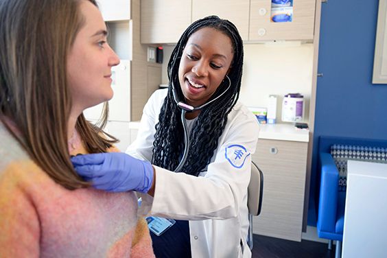An MSK clinician smiles while holding a stethoscope on a patient’s chest. 