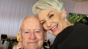 An elderly couple faces the camera, hugging and smiling.    
