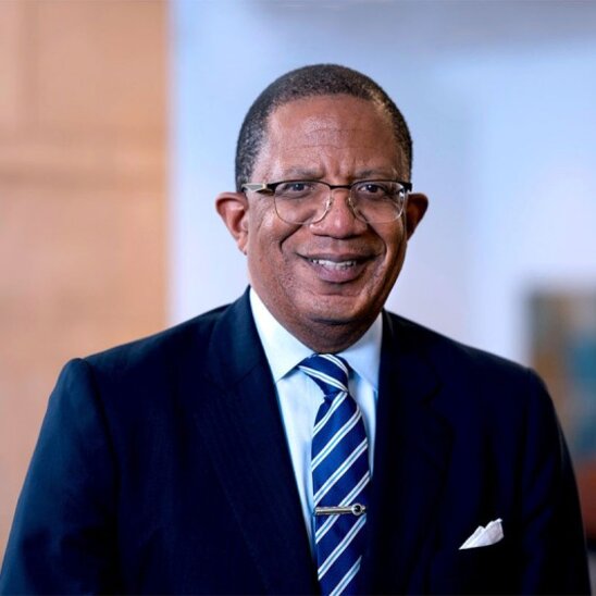 Smiling man in a suit and striped tie with a blurred background.
